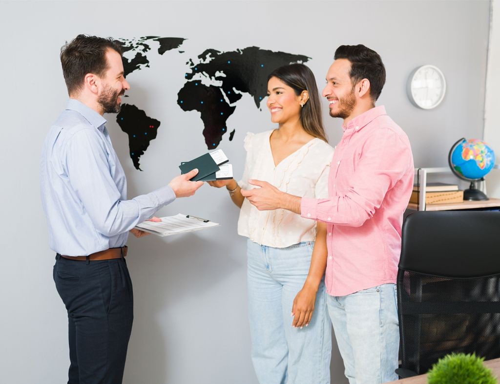 Couple receiving travel documents from a man in an office with a world map on the wall.